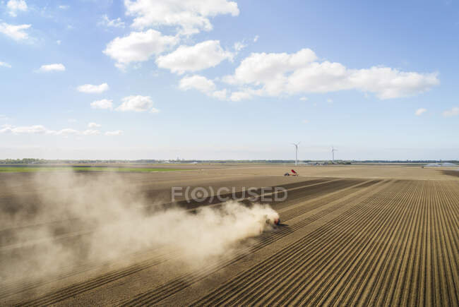 Trattore soffiando polvere sulla siccità campo di patate colpite nei Paesi Bassi, cielo con nuvole — Foto stock