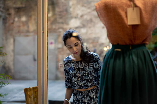 Woman with long black hair looking at skirt on mannequin in shop window. — Stock Photo