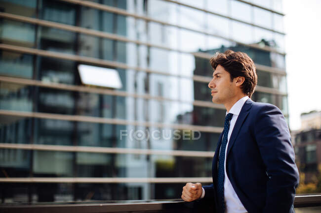 Businessman wearing blue suit walking past glass facade of office building. — Stock Photo