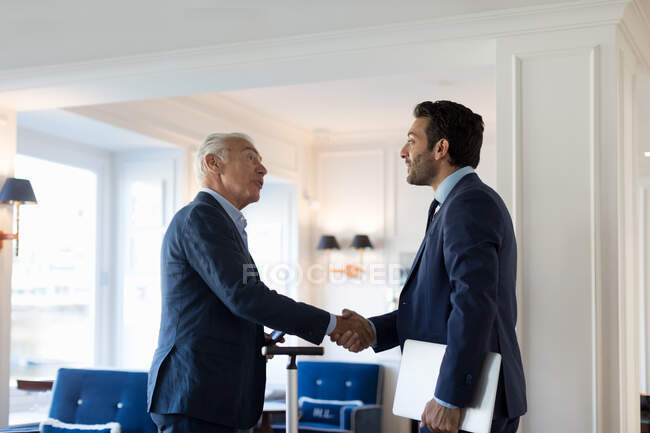 Dois homens de negócios em pé dentro de casa, apertando as mãos. — Fotografia de Stock