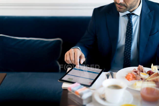 Geschäftsmann schaut beim Arbeitsessen auf sein digitales Tablet. — Stockfoto