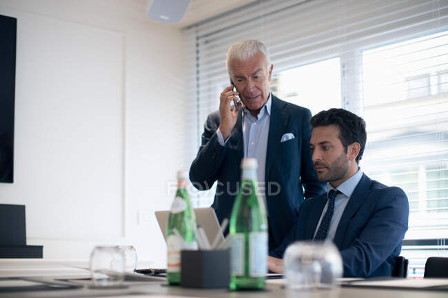 Dois empresários em um escritório, digitando no laptop e usando telefone celular. — Fotografia de Stock