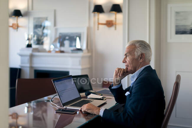Старший бізнесмен сидить за столом, дивлячись на ноутбук . — стокове фото