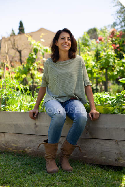 Retrato de una mujer sonriente con el pelo largo y castaño sentado en un jardín. - foto de stock