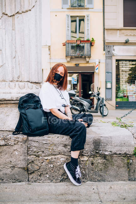 Young woman wearing face mask during Corona virus, sitting outdoors, looking at camera. — Stock Photo
