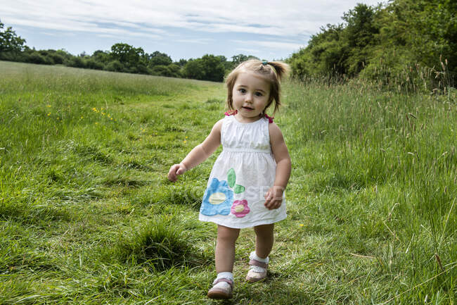Portrait de jeune fille en robe blanche marchant sur une prairie, regardant la caméra. — Photo de stock