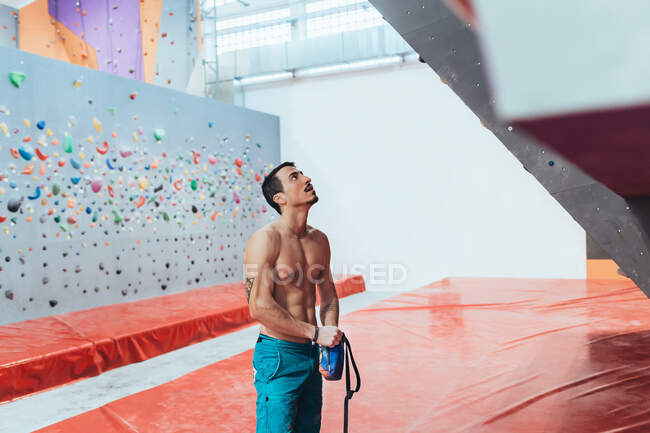 Ein muskulöser Mann mit nacktem Oberkörper steht vor einer Kletterwand. — Stockfoto
