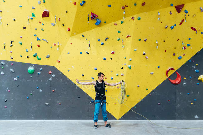 Man holding long rope standing in front of indoor rock climbing wall. — Stock Photo