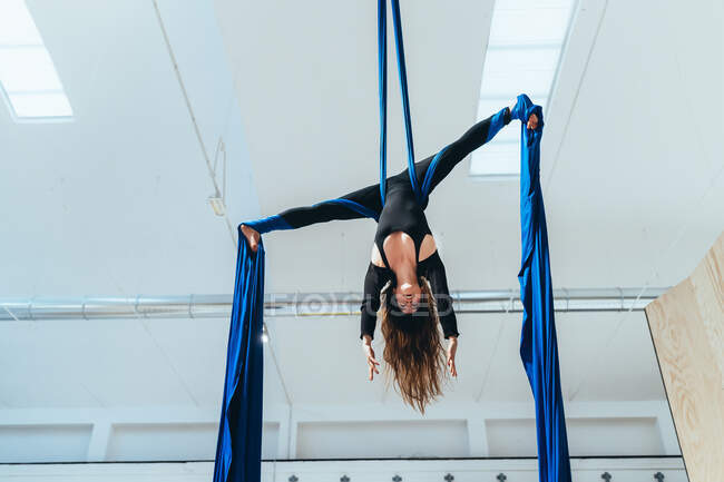 Female acrobat aerialist practicing, suspended from a length of blue silk — Stock Photo