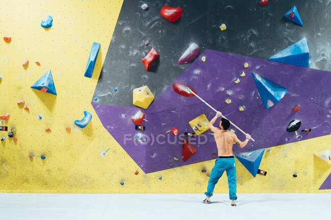 Rear view of man brushing rock climbing wall with broom. — Stock Photo