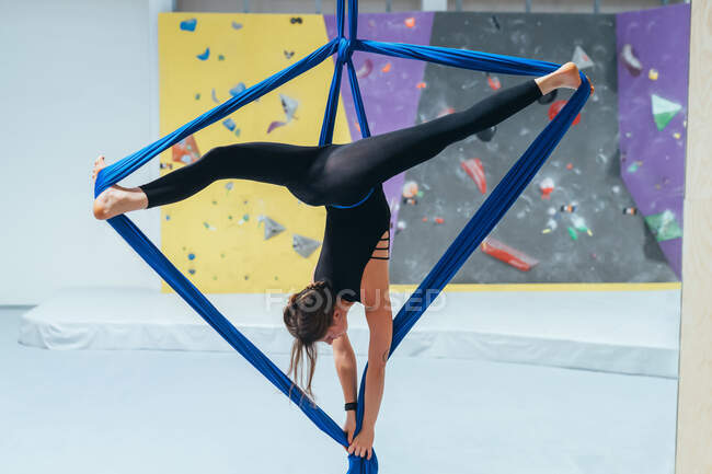Aerialista acrobata fêmea praticando, suspensa de um comprimento de seda azul — Fotografia de Stock