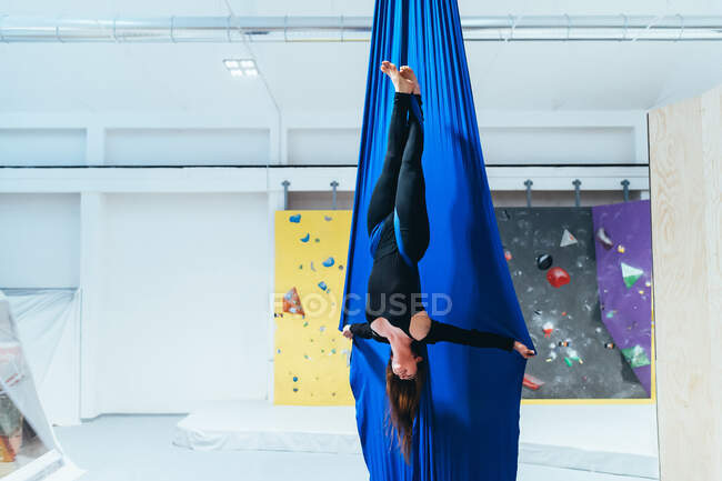 Female acrobat aerialist practicing, suspended from a length of blue silk — Stock Photo