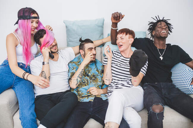Grupo de jovens homens e mulheres sentados em um sofá, rindo — Fotografia de Stock