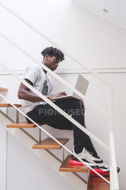Jeune homme avec de courtes dreadlocks assis sur l'escalier, dactylographiant sur ordinateur portable portable portable — Photo de stock