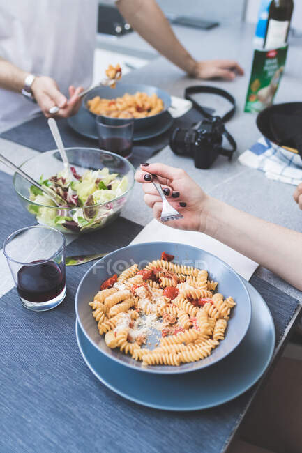High angle close up of two people hands at a table, eating from bowls of Fusilli pasta — Stock Photo