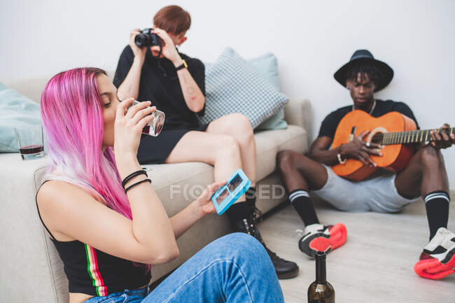 Groupe de jeunes amis dans l'appartement, jouer de la musique, boire du vin et prendre des photos — Photo de stock