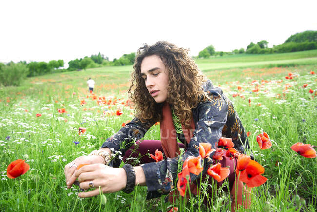 Portrait of young man with long brown curly hair in poppies meadow — Stock Photo
