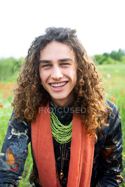 Uomo sorridente, Ritratto di giovane con lunghi capelli castani ricci nel prato dei papaveri — Foto stock
