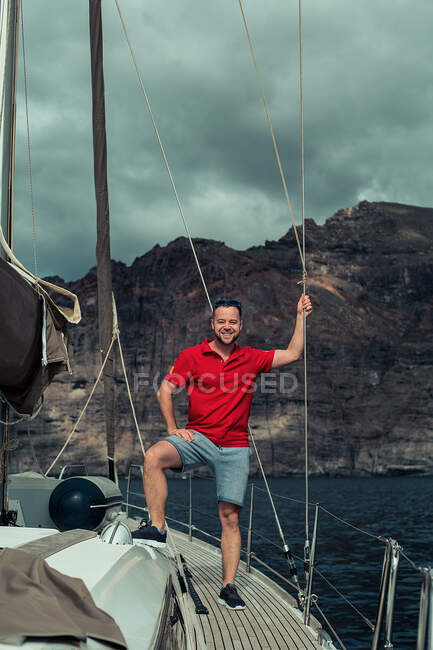 Retrato del hombre sonriente de pie a bordo de un yate de vela, cielo lluvioso y nublado - foto de stock