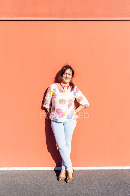 Portrait of senior woman with brown hair standing in front of orange wall, smiling at camera. — Stock Photo