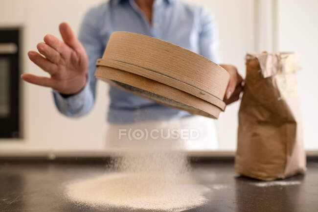 Femme debout dans une cuisine, faire des pâtes fraîches maison, tamiser la farine. — Photo de stock