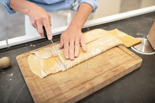 Donna in piedi in cucina, a fare tagliatelle fresche fatte in casa. — Foto stock