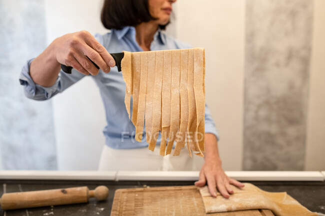 Mulher de pé em uma cozinha, fazendo macarrão tagliatelle caseiro fresco. — Fotografia de Stock