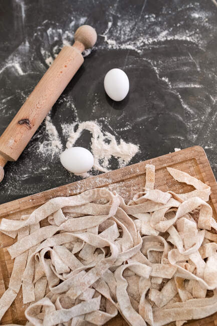 High angle close up of freshly made tagliatelle pasta on wooden cutting board. — Stock Photo