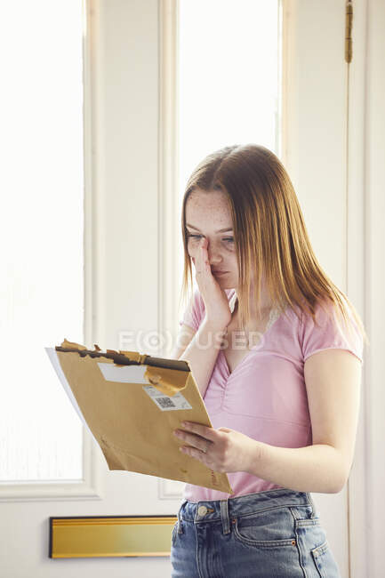 Teenage girl standing in hallway holding large envelope with letter. — Stock Photo