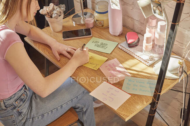 Adolescente sentada em seu quarto em uma mesa, escrevendo citações motivacionais em cartões de nota. — Fotografia de Stock