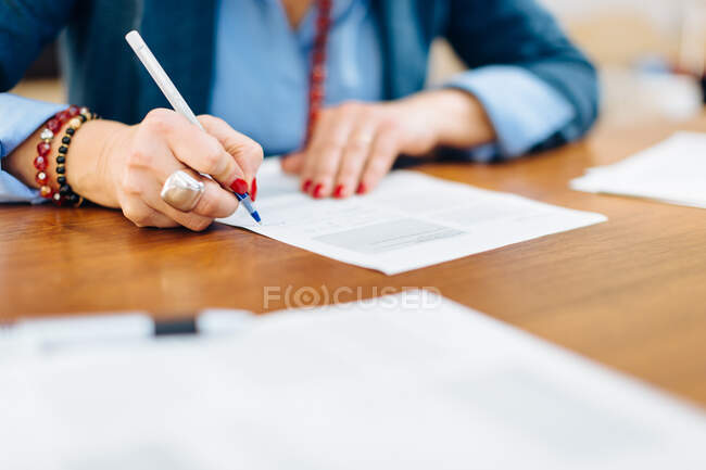 Жінка сидить за столом, пише на документі, посередині розділу, крупним планом — стокове фото