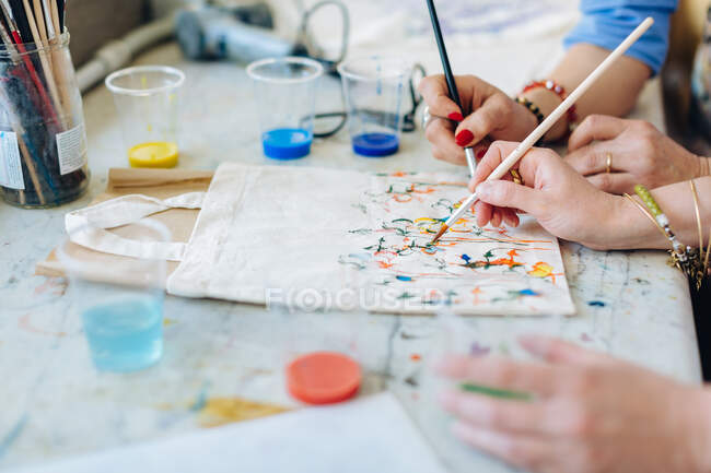 Due donne che dipingono su borsa di tessuto in studio creativo, sezione centrale, primo piano — Foto stock