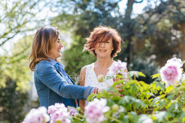 Two women laughing on rural background with flowers and trees — Stock Photo