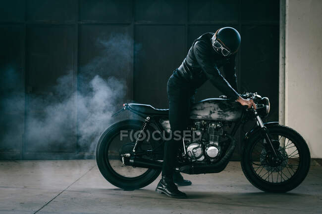 Молодий чоловічий мотоцикліст, що відновлює старовинний мотоцикл в гаражі — стокове фото