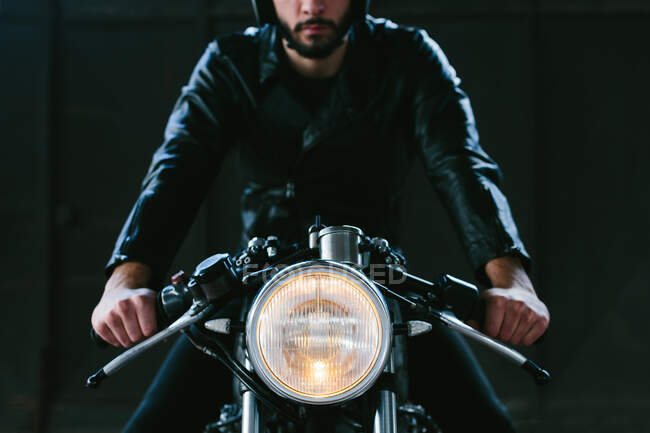 Jeune motocycliste homme chevauchant moto vintage dans le garage, vue de face recadrée — Photo de stock