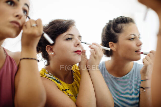 Friends putting on makeup at mirror, close-up view — Stock Photo