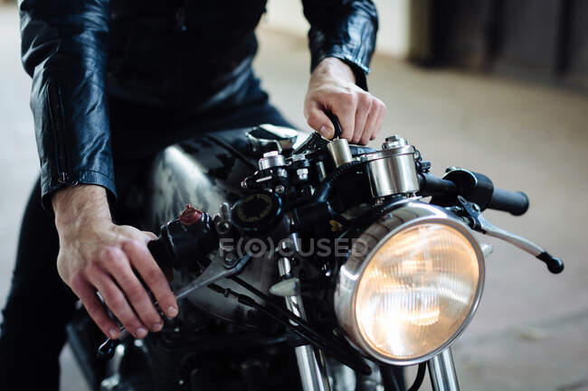 Молодий чоловічий мотоцикліст розтягує старовинний мотоцикл в гаражі, обрізаний — стокове фото