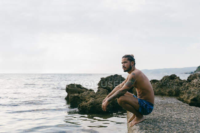 Homem sentado na praia à beira da água — Fotografia de Stock