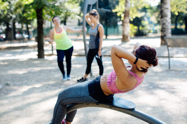 Woman doing sit ups in park, friends in background — Stock Photo