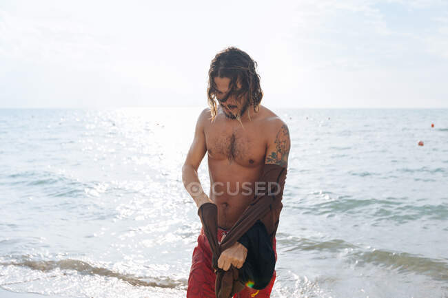 Hombre quitando ropa por mar - foto de stock