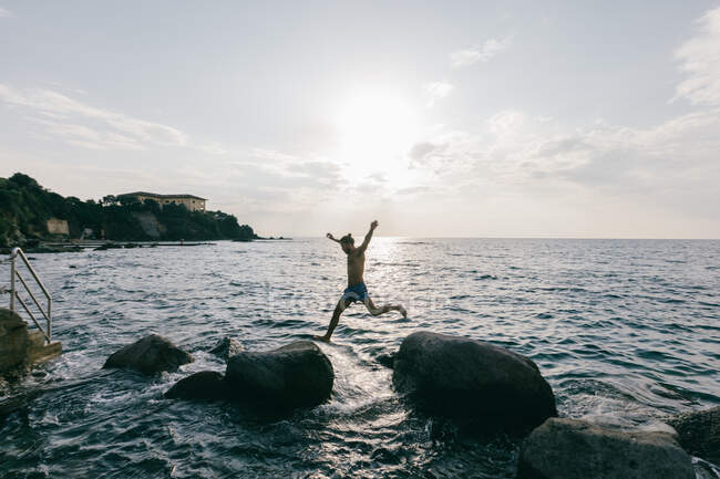 Hombre saltando de roca en roca en el mar - foto de stock