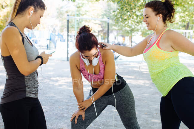 Amigos exercitando e usando celular no parque — Fotografia de Stock