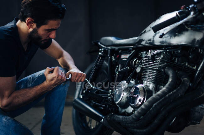 Молодий чоловічий мотоцикліст ремонтує старовинний мотоцикл в гаражі — стокове фото