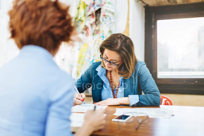 Dos mujeres sentadas a la mesa, trabajando, en un taller creativo - foto de stock