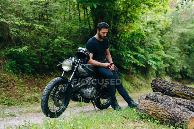 Joven motociclista masculino en motocicleta vintage en carretera rural mirando el teléfono inteligente, Florencia, Toscana, Italia - foto de stock