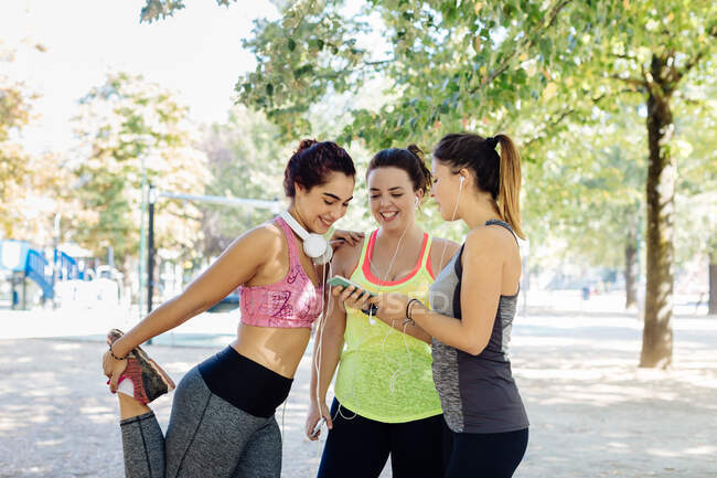 Friends exercising and using cellphone in park, close-up view — Stock Photo