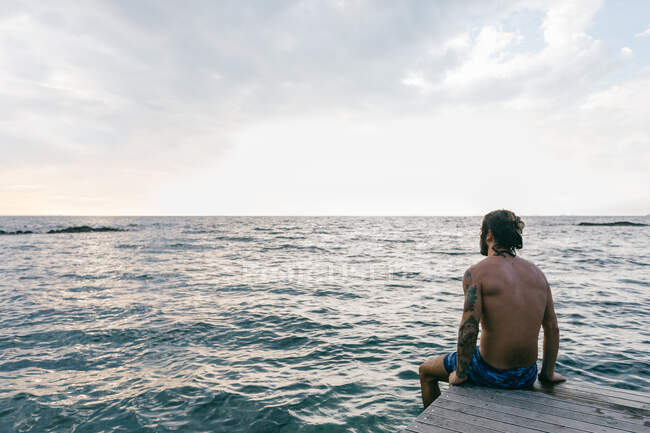 Uomo seduto sul bordo del mare — Foto stock