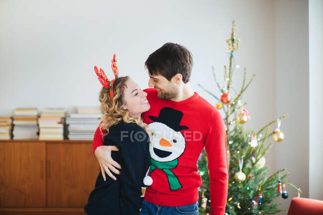 Casal abraçando na frente da árvore de Natal em casa — Fotografia de Stock