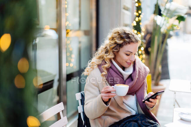 Femme utilisant un smartphone et prenant une boisson chaude au café, Firenze, Toscane, Italie — Photo de stock