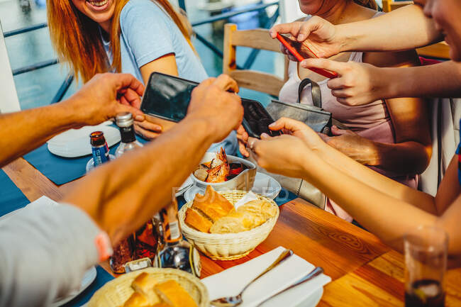 Um grupo de pessoas sentadas à mesa redonda, tirando fotos de pratos de comida com telefones inteligentes — Fotografia de Stock